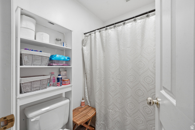 203 North Geneva Road, Unit 10 Provo, UT 84601 - Photo 9 of 30 Compact bathroom featuring a white toilet with an integrated over-toilet shelving unit, a shower area with a black rod, and a paneled interior door with a polished chrome knob