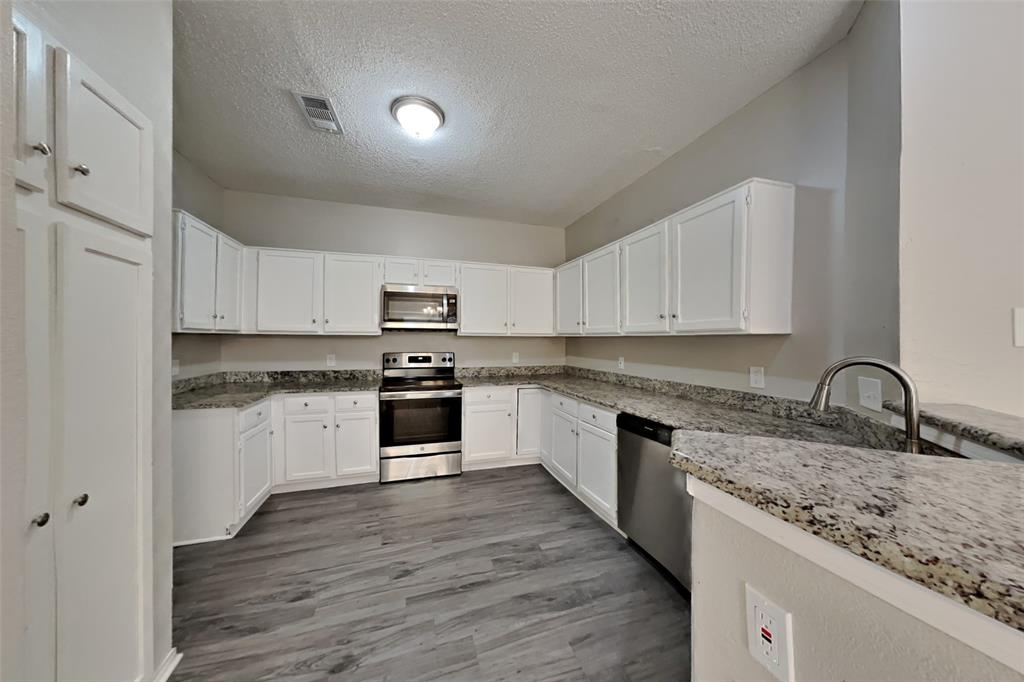 921 Mossberg Lane Mesquite, TX 75181 - Photo 5 of 17 Kitchen with stainless steel appliances, a textured ceiling, dark wood-type flooring, white cabinetry, and light stone countertops