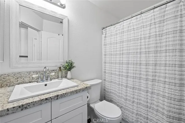 a bathroom with a granite countertop toilet a sink a mirror and shower curtain