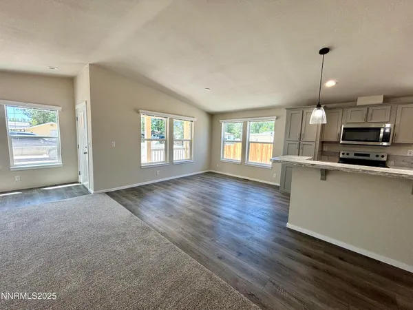 a view of an empty room with kitchen and window