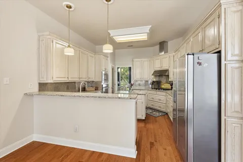 a kitchen with stainless steel appliances granite countertop a refrigerator a oven a sink and white cabinets with wooden floor