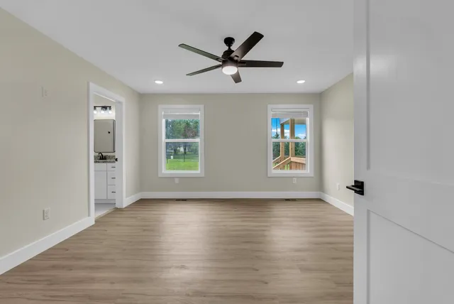 an empty room with wooden floor a ceiling fan and windows