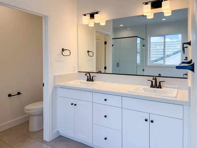 a bathroom with a double vanity sink and mirror with toilet