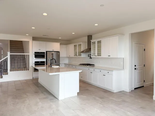 a large white kitchen with kitchen island a sink a stove and a refrigerator with wooden floor