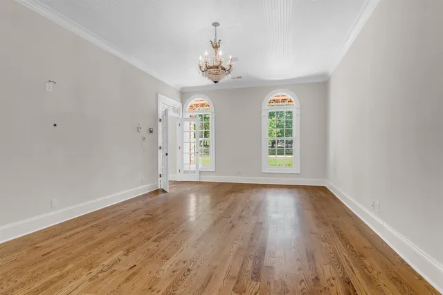 an empty room with wooden floor chandelier and windows