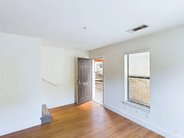 a view of an empty room with wooden floor and a window