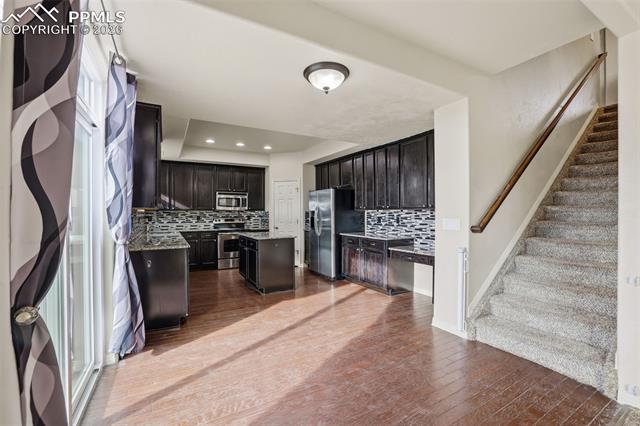 2224 Reed Grass Way Colorado Springs, CO 80915 - Photo 15 of 39 Kitchen featuring a kitchen island, stainless steel appliances, backsplash, dark wood-style flooring, and light stone countertops