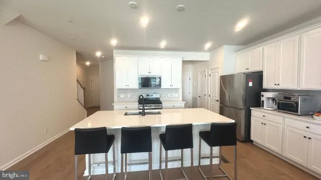 a kitchen with stainless steel appliances kitchen island granite countertop a dining table chairs refrigerator and microwave