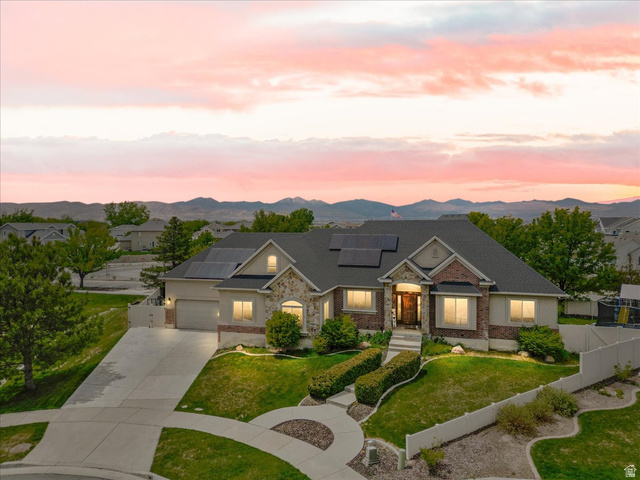 316 Azure Circle Draper, UT 84020 - Photo 3 of 48 Exterior featuring a stone and brick facade, a multi-car driveway, a covered entry, a dark roof with solar panels, and mature landscaping
