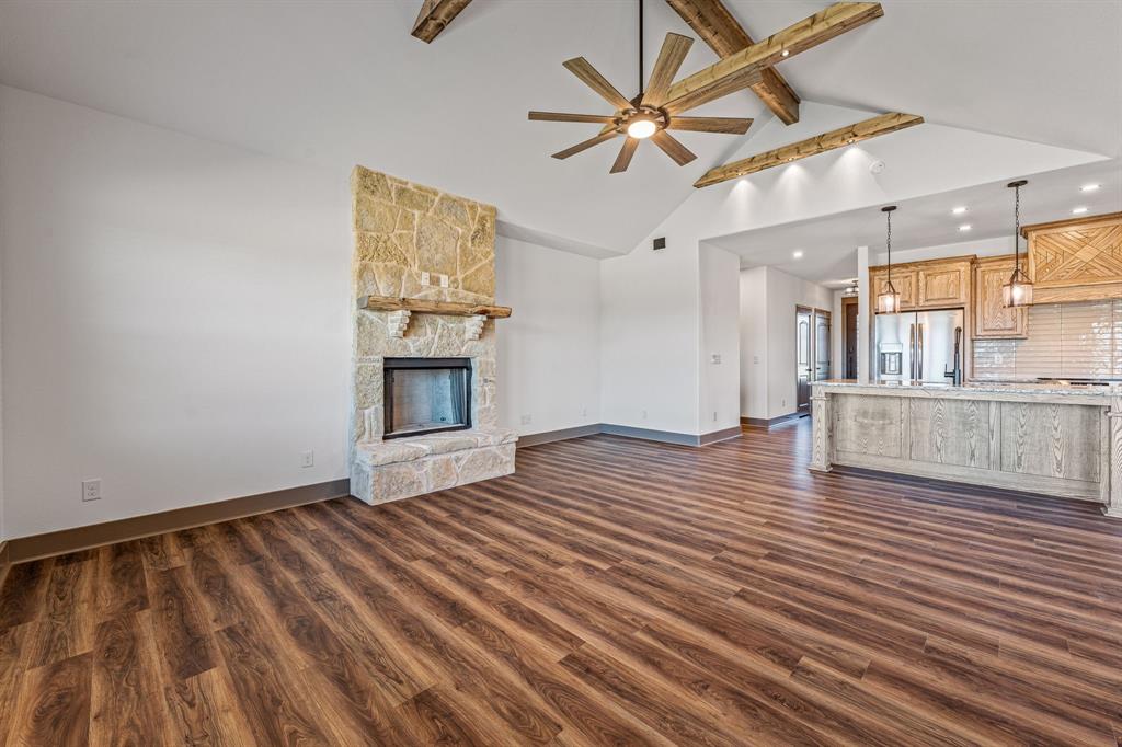 1035 Barton Ranch Road Nemo, TX 76070 - Photo 9 of 28 Unfurnished living room featuring beamed ceiling, dark wood-type flooring, a ceiling fan, a fireplace, and high vaulted ceiling