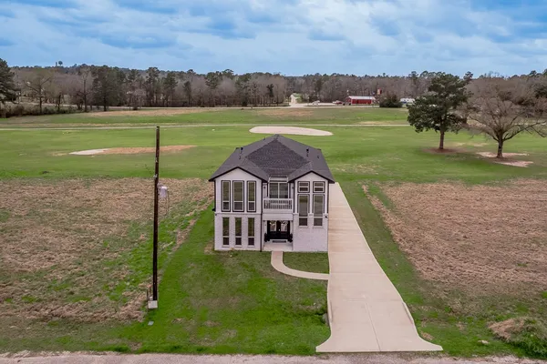 a view of a white house in front of a big yard with plants and large trees