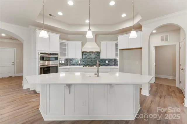 a large kitchen with kitchen island a large counter top a sink stainless steel appliances and cabinets