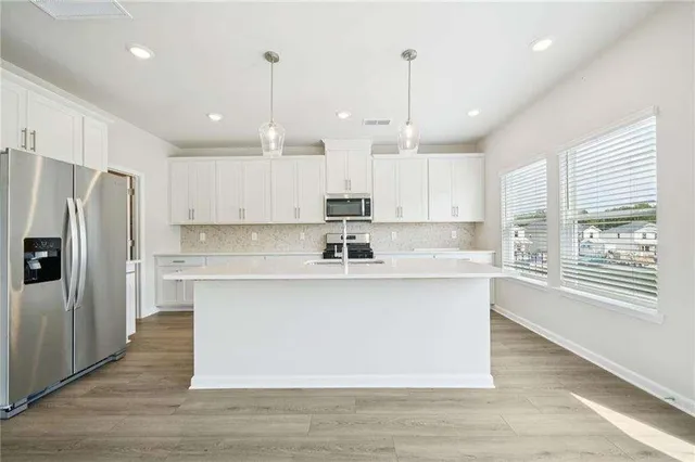 a large kitchen with stainless steel appliances granite countertop a sink a oven a refrigerator and white cabinets with wooden floor