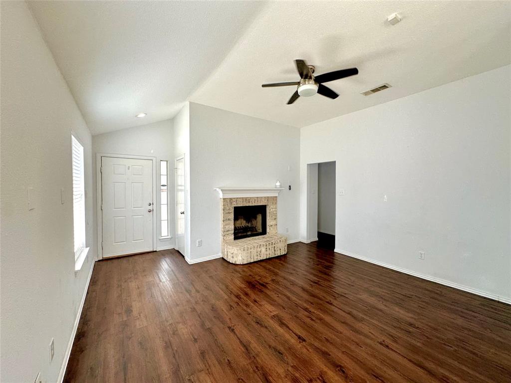 an empty room with wooden floor a ceiling fan a fireplace and windows
