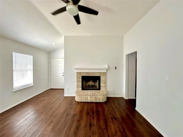a view of an empty room with wooden floor fireplace and a window