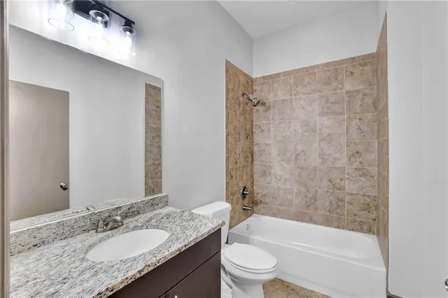 a bathroom with a granite countertop bathtub shower sink vanity mirror and toilet
