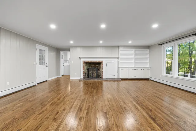 an empty room with wooden floor fireplace and windows