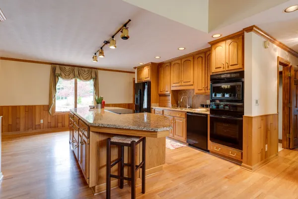 a kitchen with stainless steel appliances kitchen island granite countertop a stove a refrigerator a sink a dining table and chairs with wooden floor