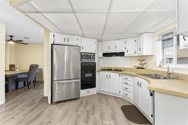 a kitchen with granite countertop a refrigerator oven a sink dishwasher and white cabinets with wooden floor