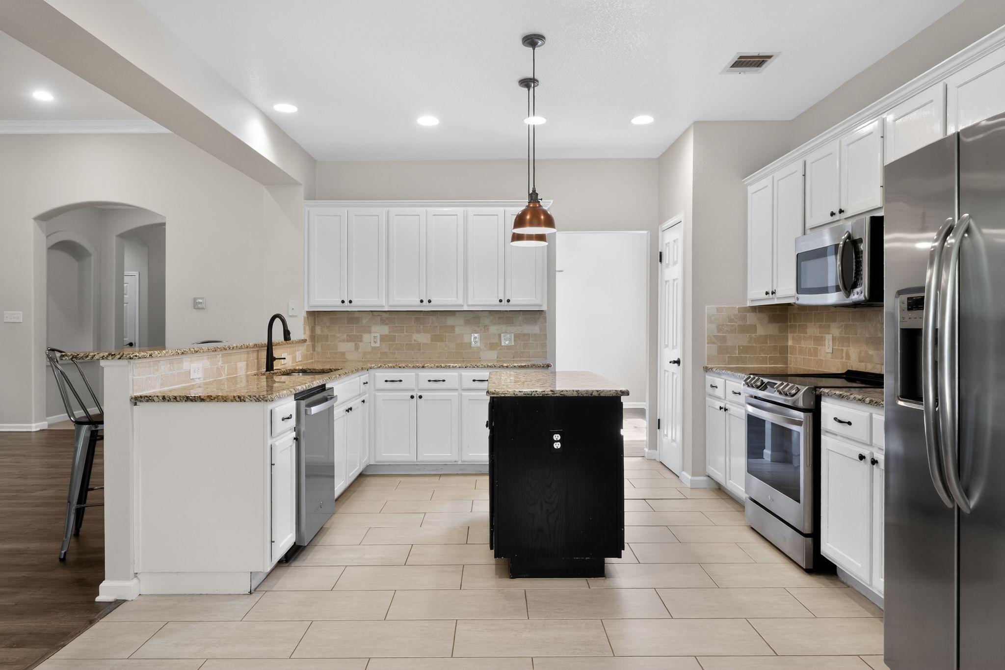 11918 Arbor Downs Road Austin, TX 78748 - Photo 13 of 29 Kitchen with a peninsula, stainless steel appliances, light stone countertops, a kitchen island, and a breakfast bar