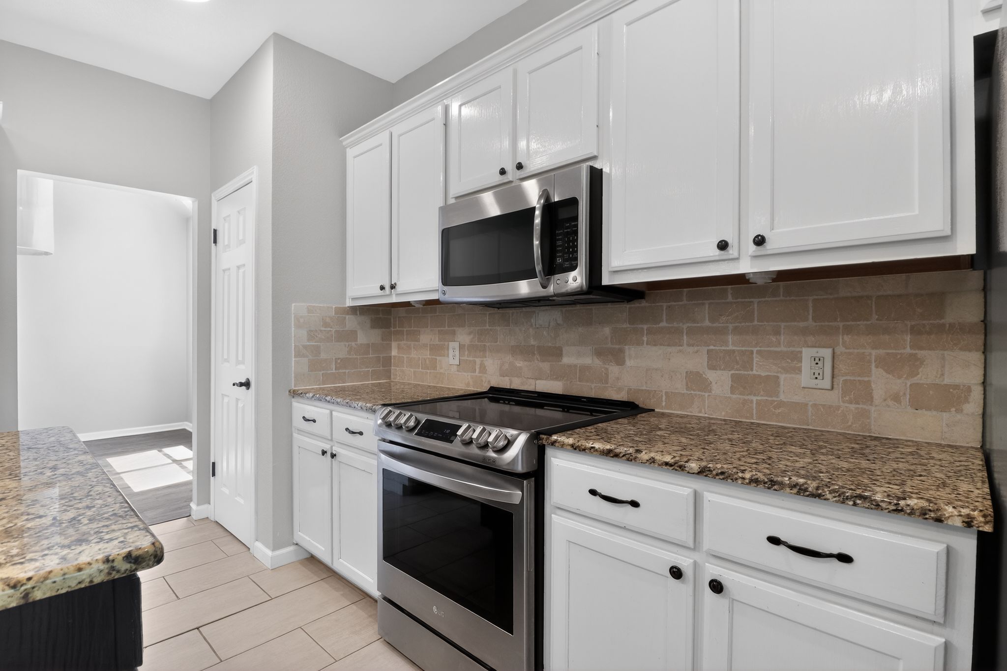 11918 Arbor Downs Road Austin, TX 78748 - Photo 16 of 29 Kitchen featuring stainless steel appliances, white cabinets, dark stone countertops, tasteful backsplash, and light tile patterned floors