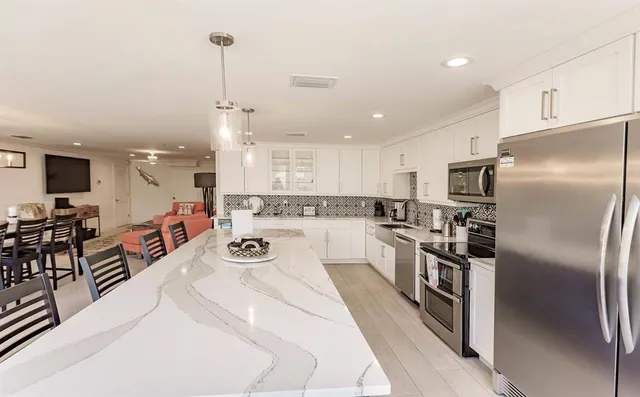 a kitchen with stainless steel appliances kitchen island granite countertop a refrigerator a stove a sink a dining table and chairs with wooden floor