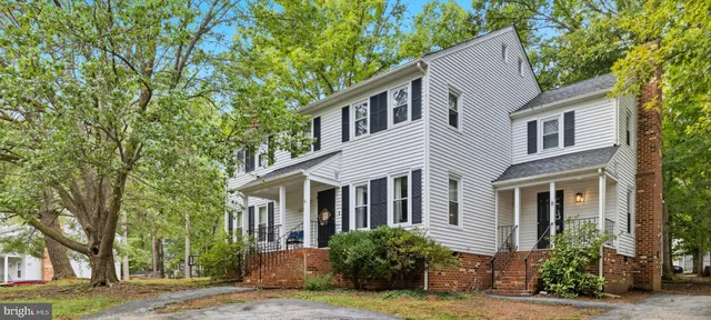 a view of a white house next to a yard with large trees