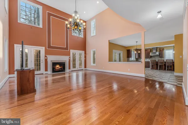 an empty room with wooden floor fireplace chandelier and windows