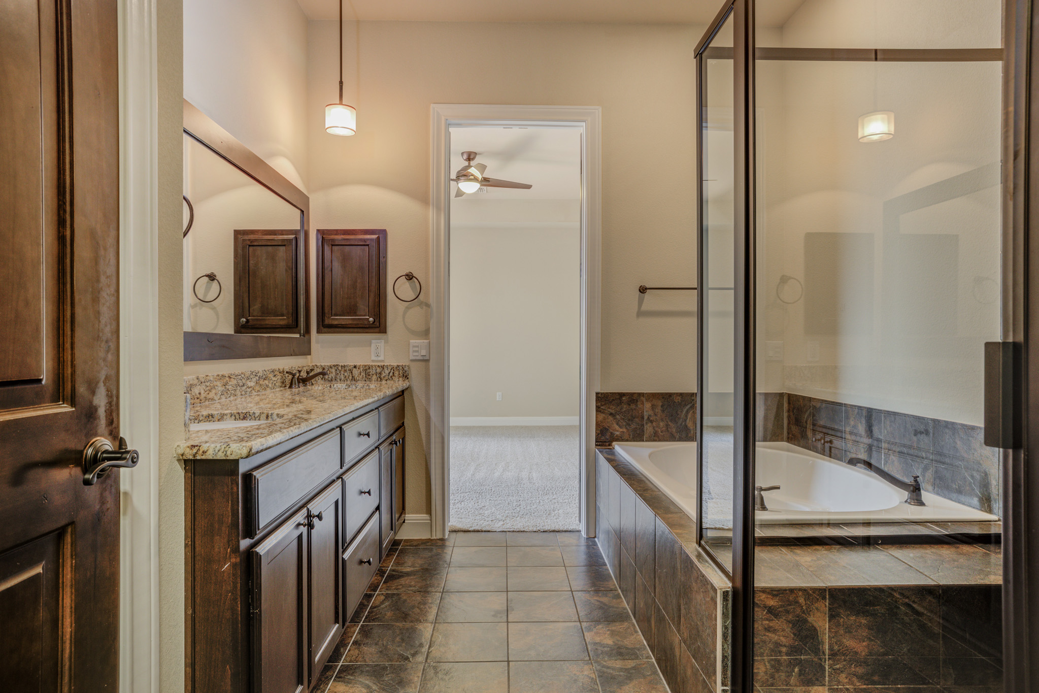 4524 Berkman Drive Austin, TX 78723 - Photo 24 of 38 Bathroom featuring a dark wood double vanity with a light-toned granite countertop, a built-in soaking tub with dark-toned tile surround, and a glass-enclosed shower