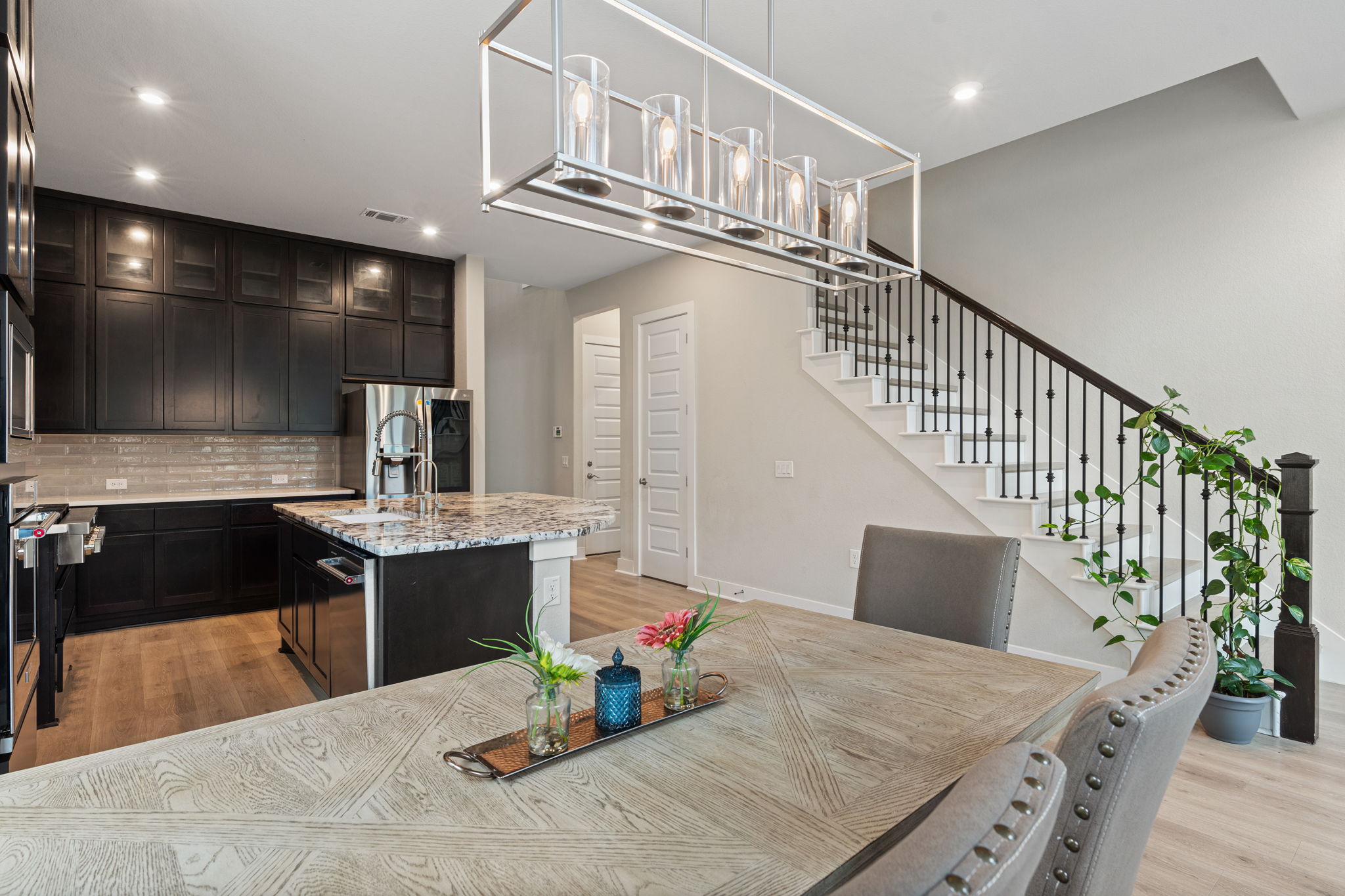 244 Diamondback Drive Georgetown, TX 78628 - Photo 13 of 37 Kitchen and dining area featuring dark cabinetry, a contemporary linear chandelier, and a staircase with wrought iron balusters.