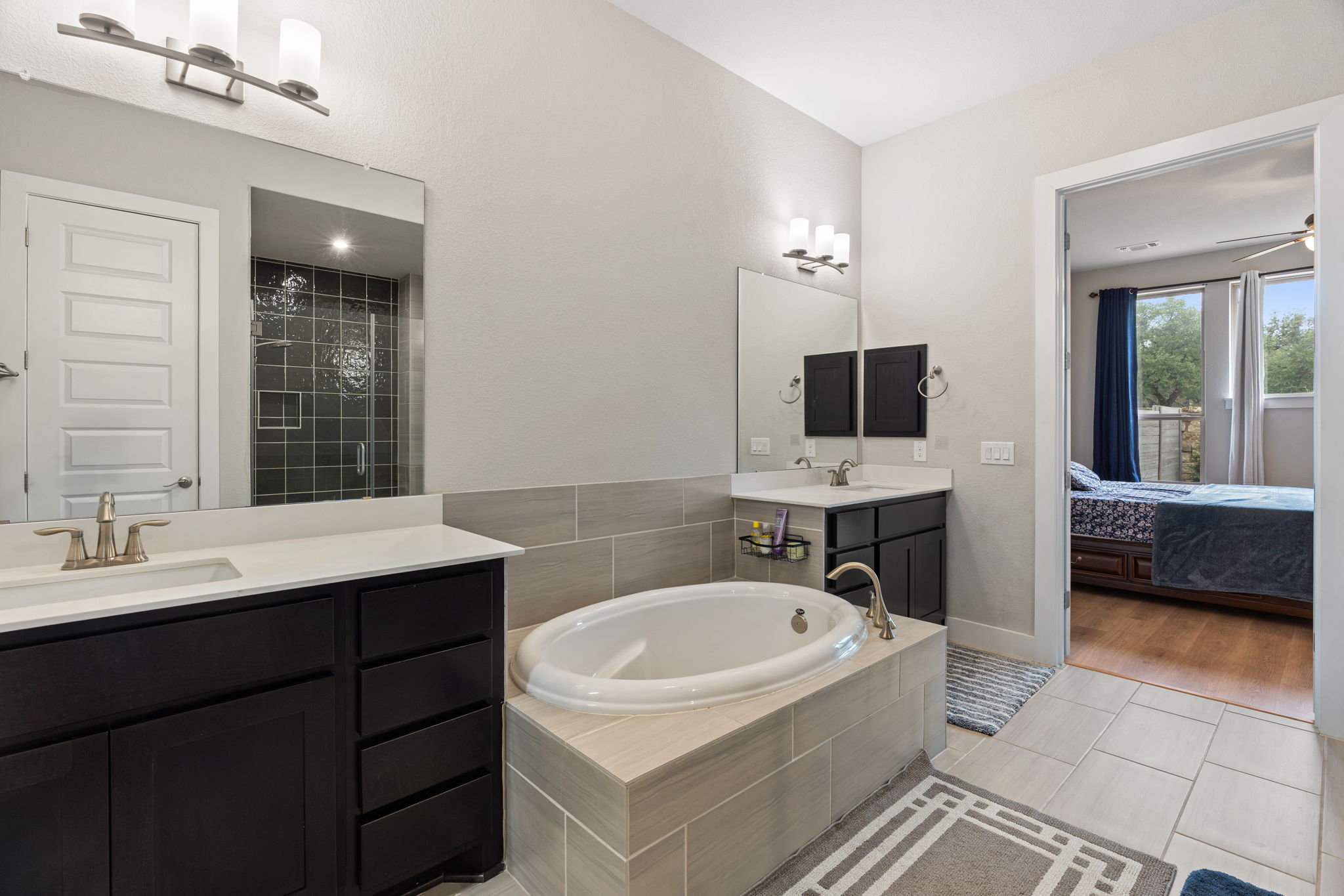244 Diamondback Drive Georgetown, TX 78628 - Photo 21 of 37 Bathroom with dual vanities, a built-in soaking tub, a tiled shower enclosure with glass door, and neutral-toned wall and floor tiling