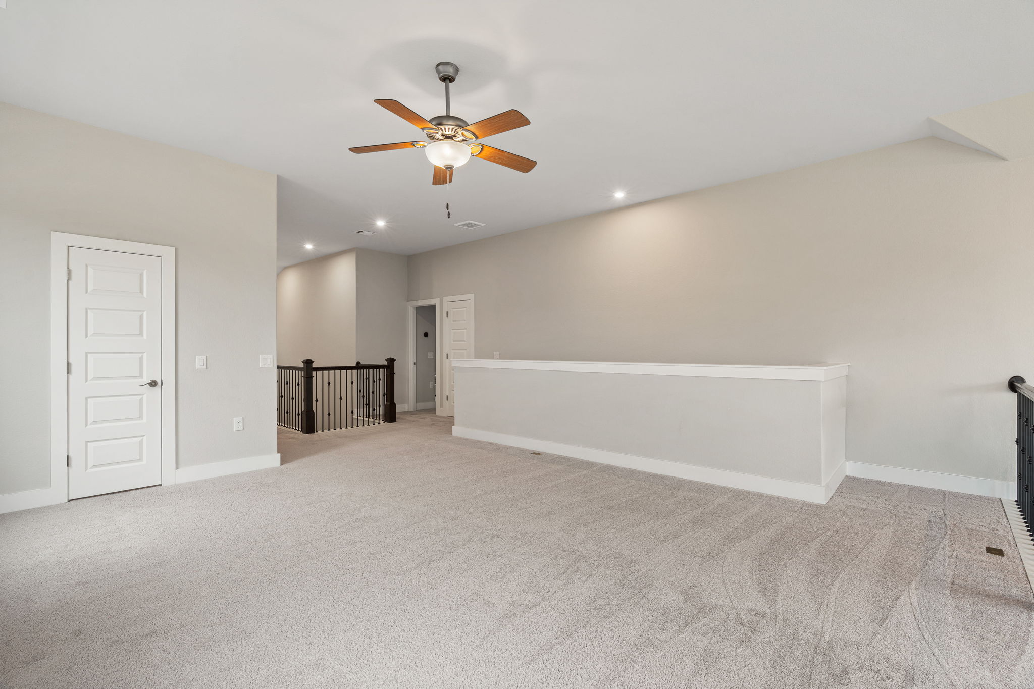 244 Diamondback Drive Georgetown, TX 78628 - Photo 27 of 37 Spacious carpeted open area featuring a ceiling fan with light fixture, recessed lighting, a five-panel interior door, and a staircase with dark wood newel posts and metal balusters.