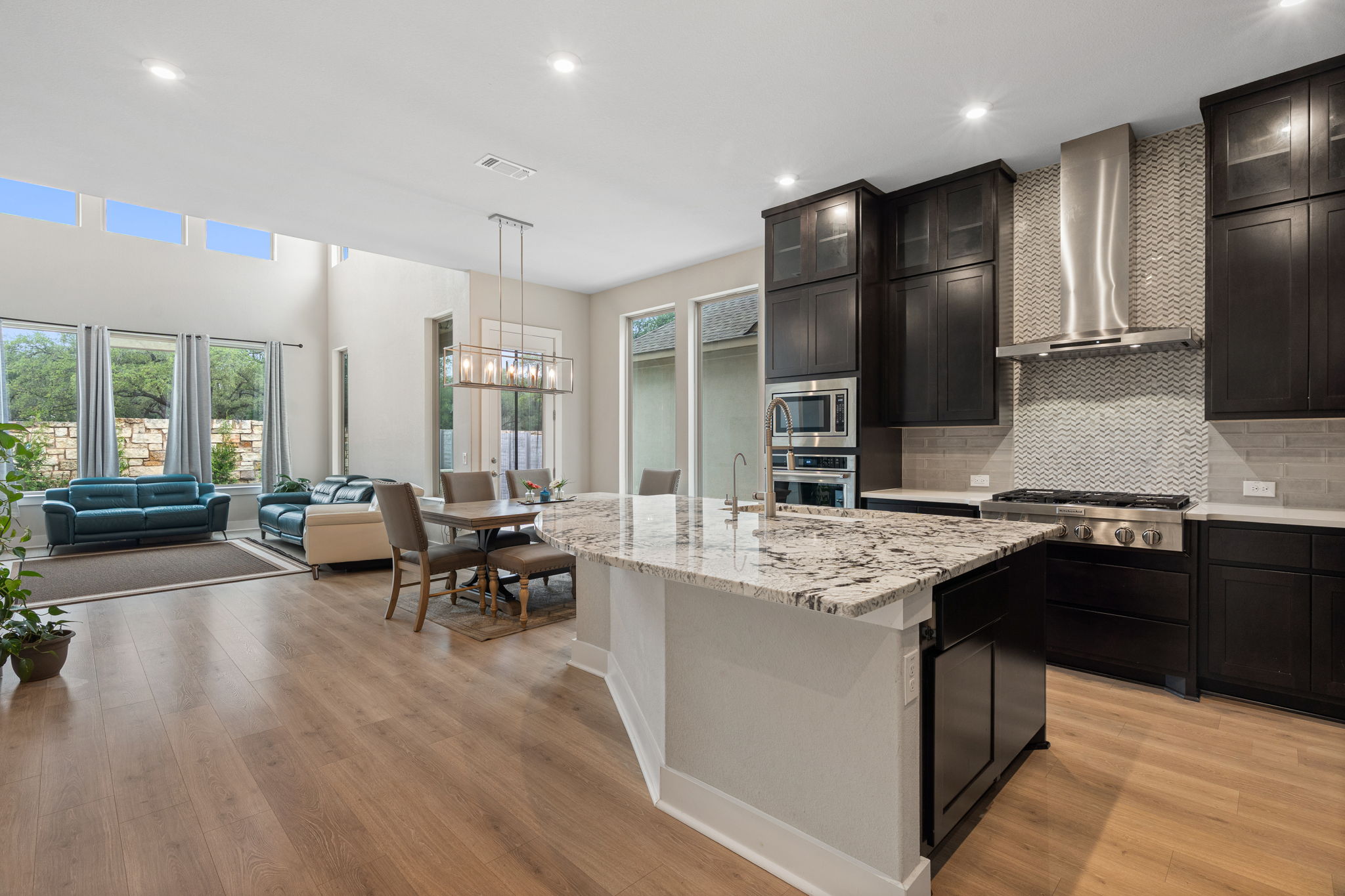 244 Diamondback Drive Georgetown, TX 78628 - Photo 3 of 37 Open-concept kitchen featuring an island with a light-toned countertop, dark wood-finish cabinetry, stainless steel appliances, and wood-finish flooring.