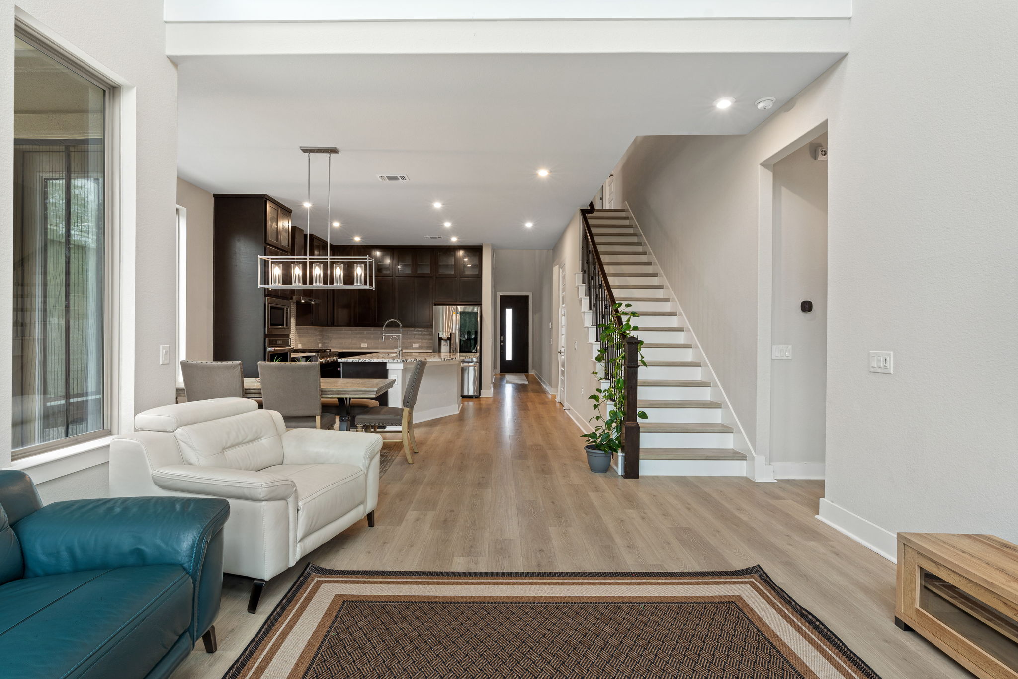 244 Diamondback Drive Georgetown, TX 78628 - Photo 5 of 37 Open-concept living area featuring wood-finish flooring, recessed lighting, a modern chandelier, dark cabinetry, and a staircase with a dark wood handrail.