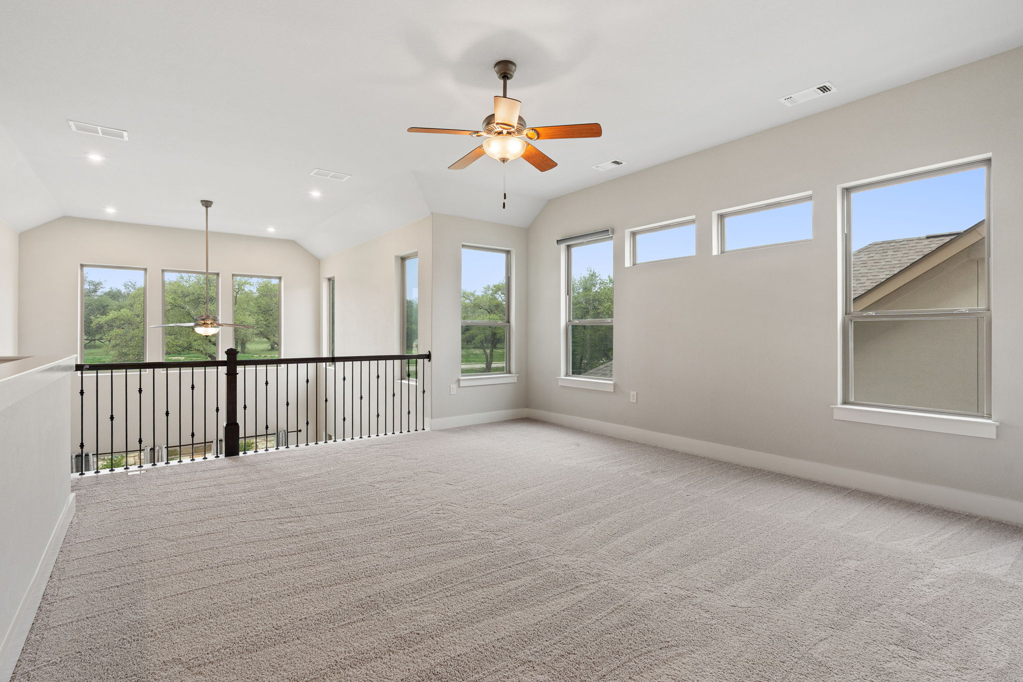 244 Diamondback Drive Georgetown, TX 78628 - Photo 7 of 37 Spacious carpeted loft area featuring multiple windows, a ceiling fan with integrated lighting, recessed lighting, and an iron baluster railing overlooking the lower level.