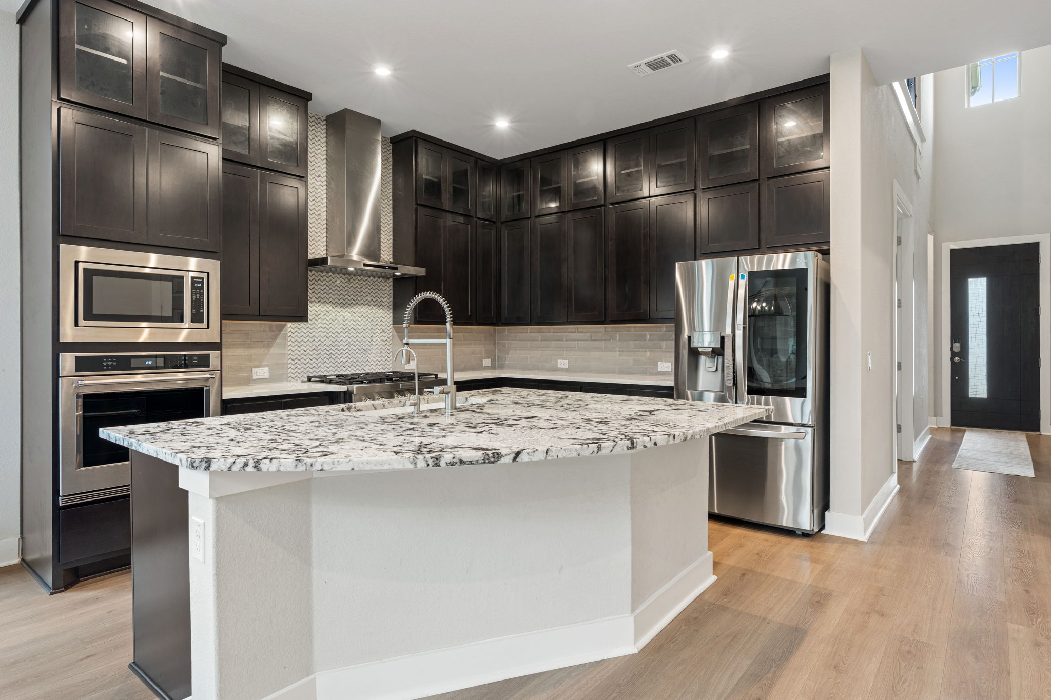 244 Diamondback Drive Georgetown, TX 78628 - Photo 10 of 37 Modern kitchen featuring dark wood cabinetry, a large central island with a light-toned patterned countertop, stainless steel appliances.