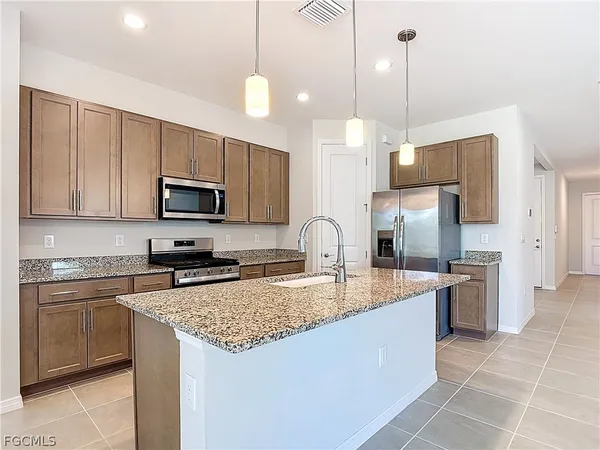 a kitchen with stainless steel appliances granite countertop a sink a stove a refrigerator a center island a stove cabinets and a kitchen island