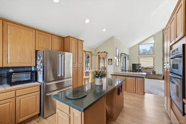 a kitchen with stainless steel appliances granite countertop a refrigerator a stove a sink a dining table and chairs with wooden floor
