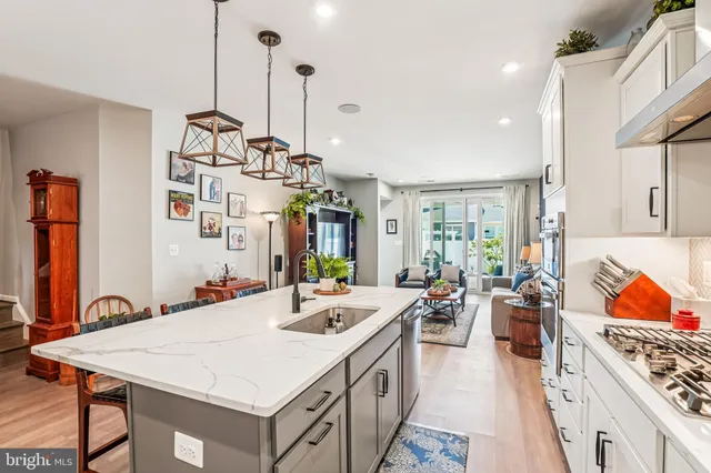 a kitchen with stainless steel appliances a stove a sink a oven a refrigerator white cabinets and couches with wooden floor