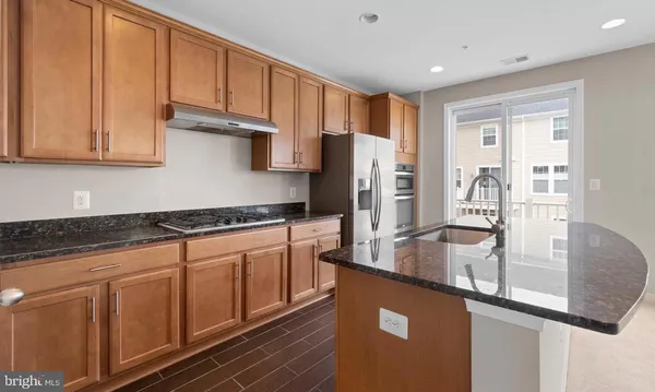a kitchen with stainless steel appliances granite countertop a refrigerator a stove and a sink with wooden cabinets