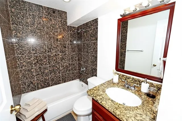 a bathroom with a granite countertop bathtub sink vanity mirror and toilet