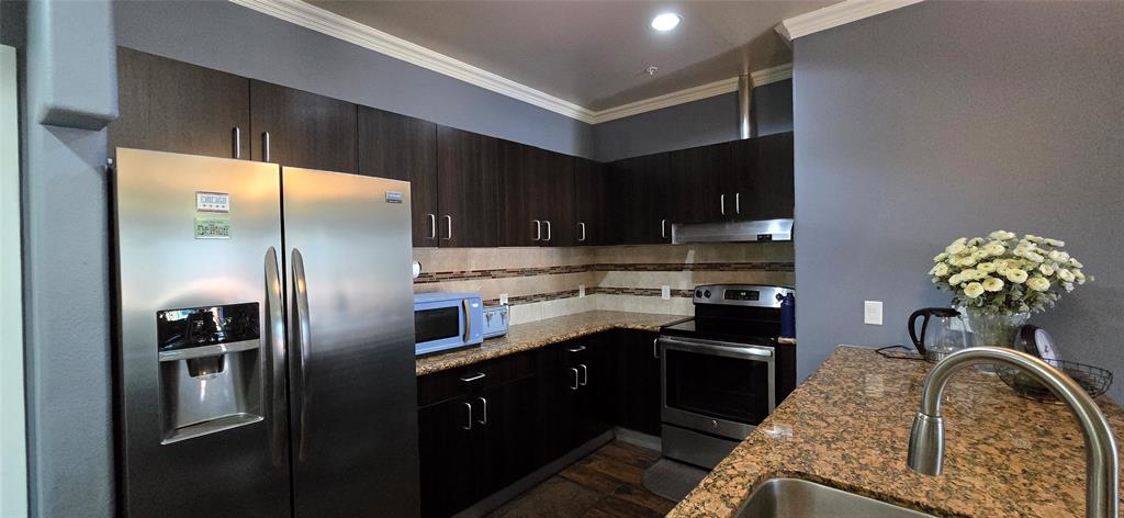 1100 West Trinity Mills Road, Unit 2045 Carrollton, TX 75006 - Photo 3 of 20 Kitchen with stainless steel appliances, dark stone counters, dark wood finish cabinetry, decorative backsplash, and crown molding