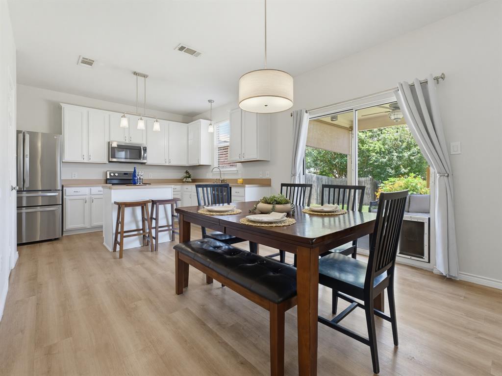 13268 Fencerow Road Fort Worth, TX 76244 - Photo 13 of 25 Bright kitchen and dining area featuring light wood-finish flooring, white cabinetry, stainless steel appliances, and a central island with pendant lighting