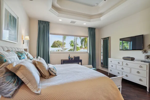 a bedroom with a bed and a flat tv screen on dresser next to a window