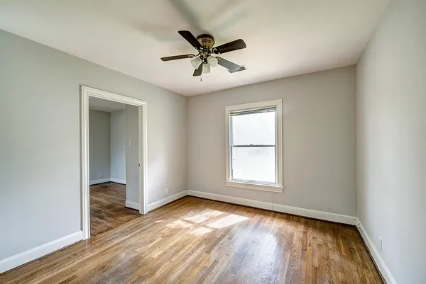 an empty room with wooden floor fan and windows