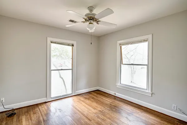 an empty room with wooden floor chandelier fan and windows