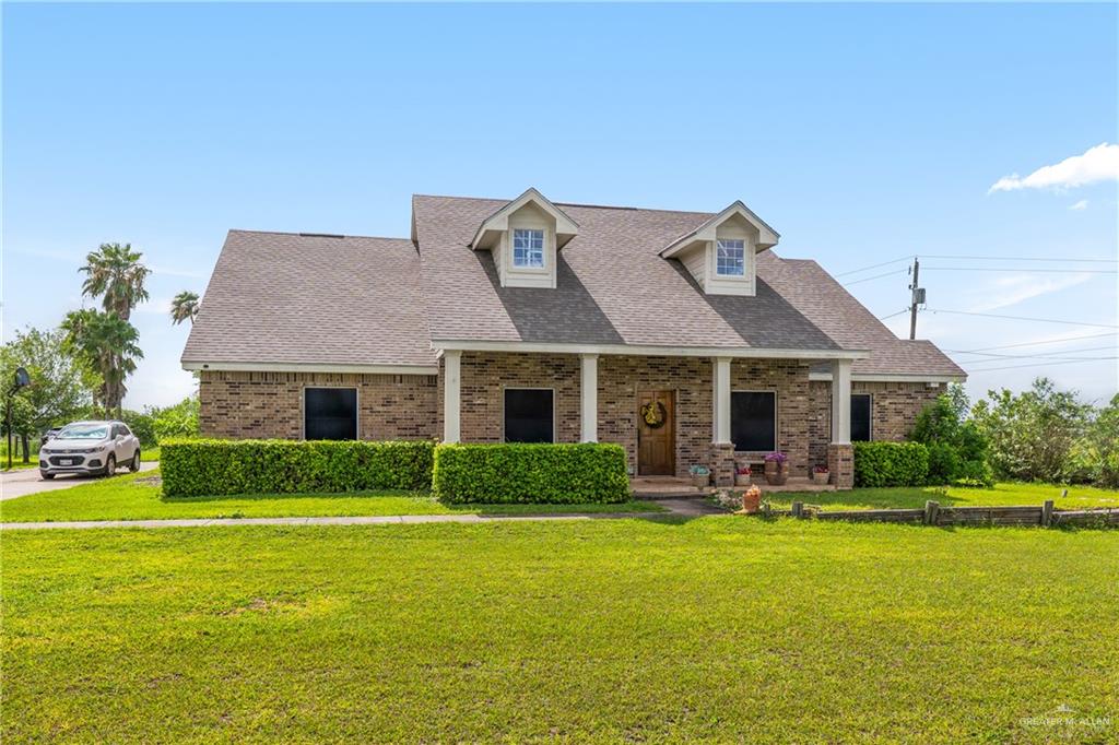 605 South Whalen Road Donna, TX 78537 - Photo 1 of 21 Brick-clad residence featuring a covered front porch with white pillars, a dark shingle roof, and twin dormer windows