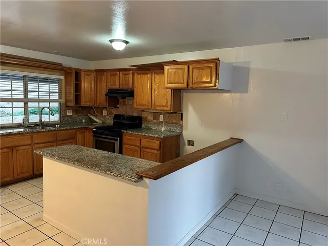 a kitchen with granite countertop a sink a stove top oven a counter space and cabinets