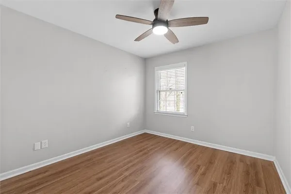 an empty room with wooden floor ceiling fan and windows