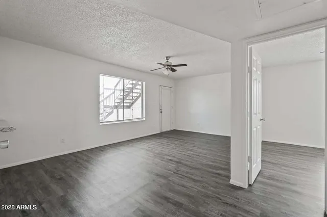 an empty room with wooden floor chandelier fan and windows